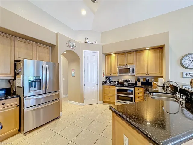 Kitchen featuring stainless steel appliances, dark stone counters, arched walkways, light tile patterned floors, and lofted ceiling