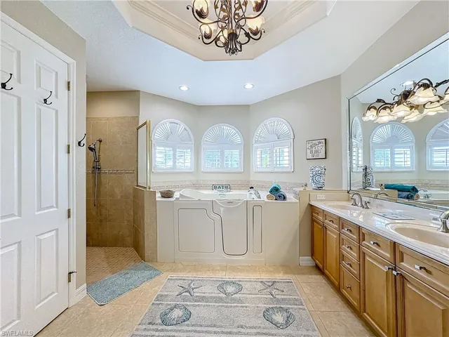 Full bath featuring a bath, walk in shower, double vanity, hanging lights, and crown molding