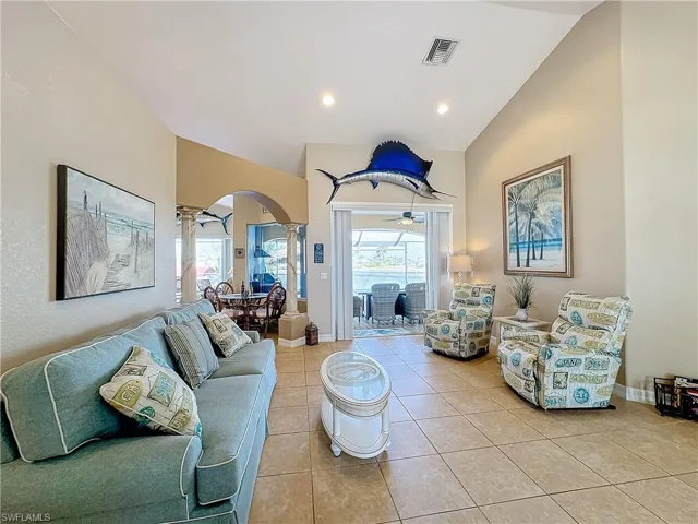 Living area featuring decorative columns, arched walkways, lofted ceiling, light tile patterned floors, and a sunroom