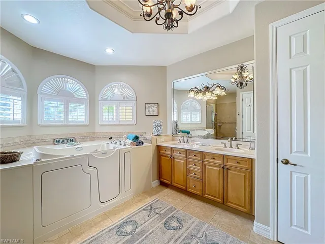 Full bath featuring a step in jetted tub, hanging lights, double vanity, and a stall shower