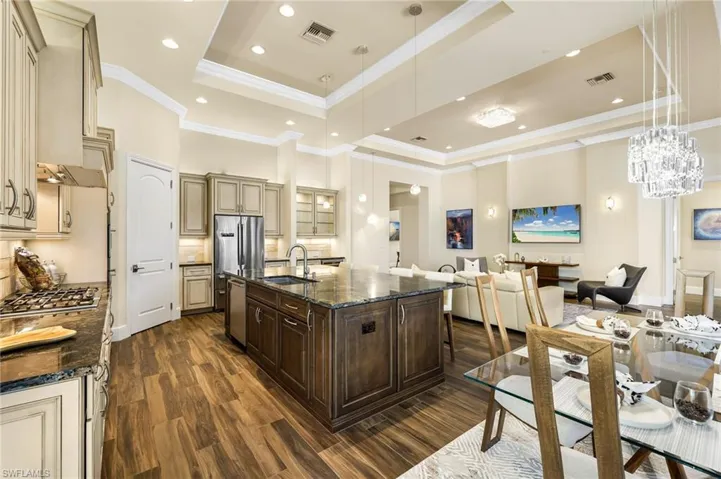 Kitchen featuring dark stone counters, cream cabinetry, a raised ceiling, and an island with sink