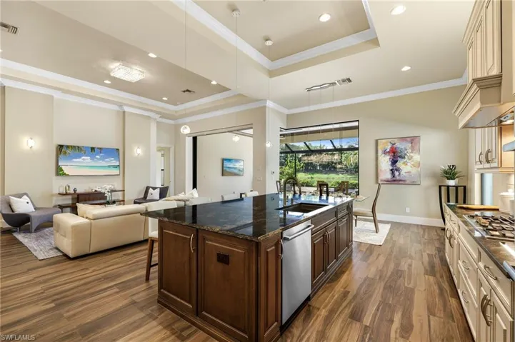 Kitchen featuring dark wood-type flooring, cream cabinetry, an island with sink, a tray ceiling, and sink