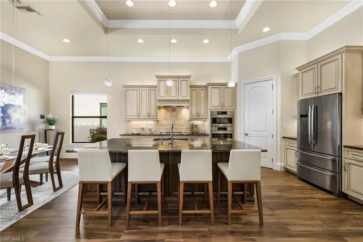 Kitchen with a kitchen bar, dark stone counters, stainless steel appliances, a center island with sink, and a tray ceiling