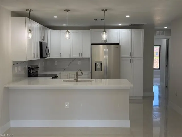 Kitchen with stainless steel appliances, a peninsula, light stone counters, white cabinetry, and backsplash