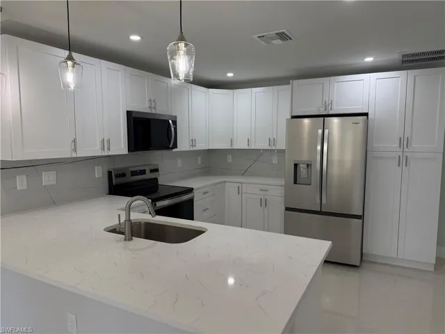Kitchen with stainless steel appliances, white cabinetry, a peninsula, light stone counters, and pendant lighting