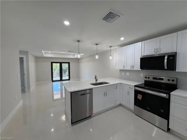 Kitchen featuring stainless steel appliances, white cabinetry, open floor plan, and decorative light fixtures