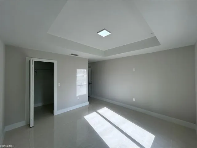 Unfurnished bedroom with a tray ceiling, a walk in closet, and light tile patterned floors