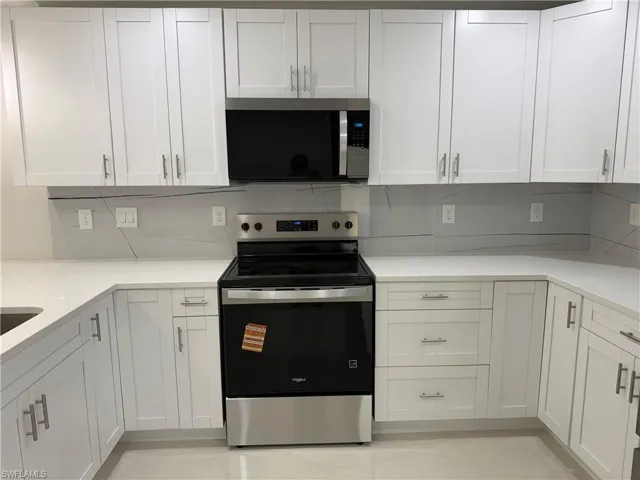 Kitchen with stainless steel appliances, white cabinets, light stone counters, and tasteful backsplash