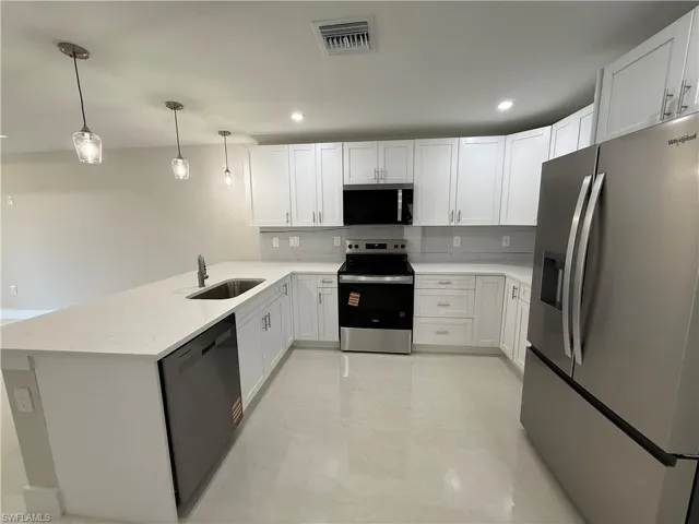 Kitchen with stainless steel appliances, a peninsula, white cabinets, pendant lighting, and light stone countertops