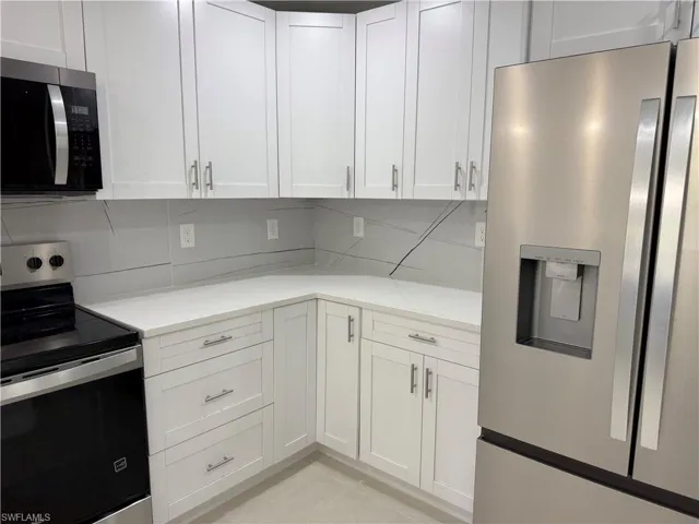 Kitchen with stainless steel appliances, light stone counters, white cabinetry, and tasteful backsplash