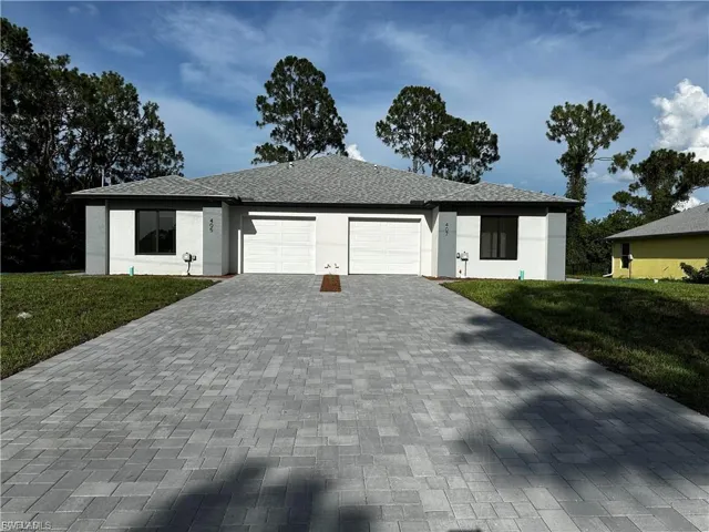 Single story home featuring a front yard, a garage, decorative driveway, and stucco siding