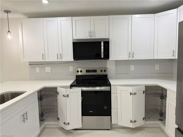 Kitchen with stainless steel appliances, white cabinetry, light stone counters, and decorative light fixtures