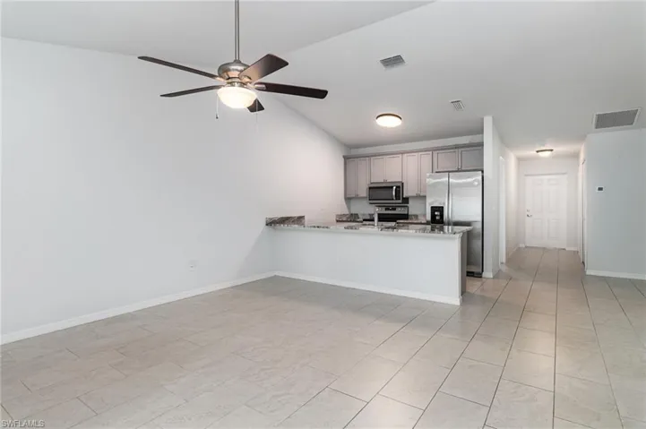 Kitchen featuring appliances with stainless steel finishes, gray cabinets, a peninsula, light stone counters, and light tile patterned floors