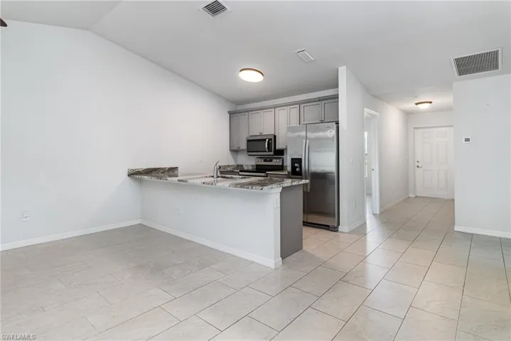 Kitchen with gray cabinetry, stainless steel appliances, a peninsula, light stone counters, and light tile patterned floors