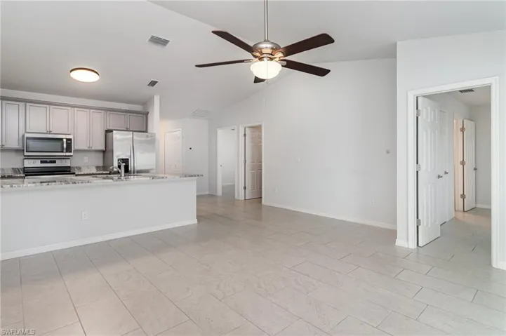 Kitchen featuring vaulted ceiling, a peninsula, stainless steel appliances, a ceiling fan, and light stone counters