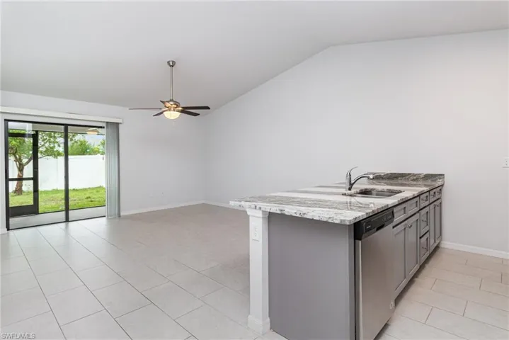 Kitchen featuring lofted ceiling, gray cabinets, stainless steel appliances, a ceiling fan, and light stone counters