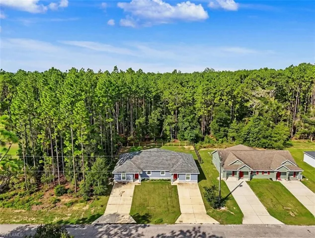 Aerial view showcasing two single-story residences situated on expansive grounds bordered by mature pine forest