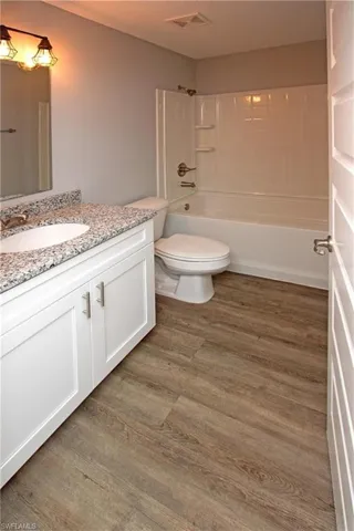 Wood-finish flooring, white vanity with granite-style countertop, white basin sink, and white shower-tub combination