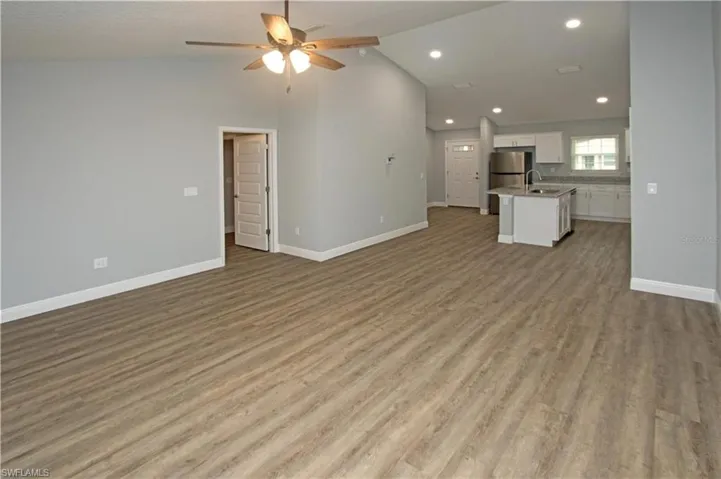 Open-concept living space with wood-finish flooring, vaulted ceiling, ceiling fan, and recessed lighting