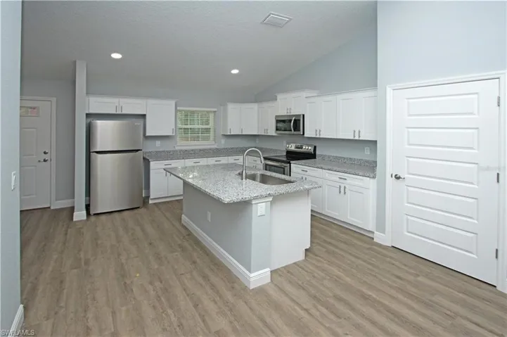 Kitchen featuring white cabinetry, a center island with a sink, stainless steel appliances, and wood-finish flooring