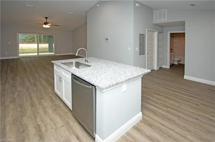 Open-concept living area featuring a kitchen island with stone-finish countertop, stainless steel appliances, and wood-finish flooring