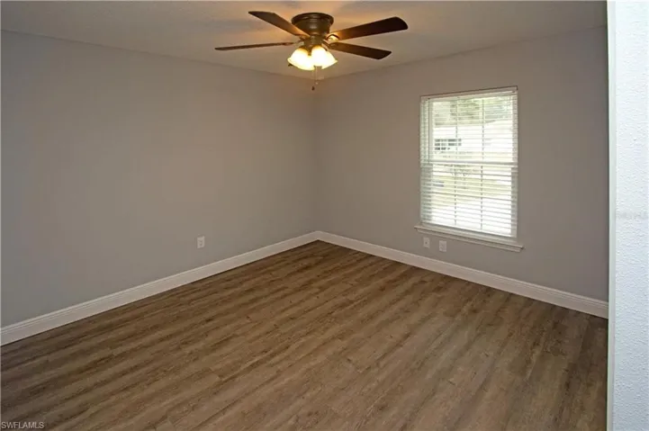 Wood-finish flooring, light grey wall paint, ceiling fan with integrated lighting, and a window with horizontal blinds