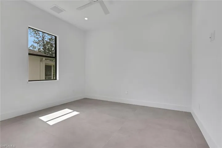 Bright room featuring large format tile flooring, a window with exterior tree-lined scenery, a ceiling fan, and recessed lighting