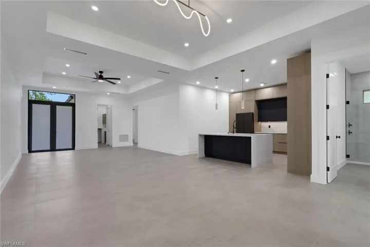 Open-concept living area with large format tile flooring and tray ceiling with recessed lighting