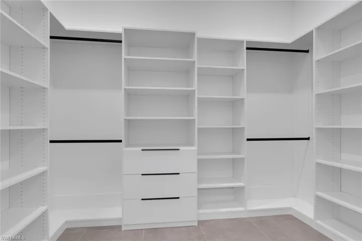 Built-in white custom closet system featuring adjustable shelving, integrated drawers with linear black pulls, and multiple hanging rods