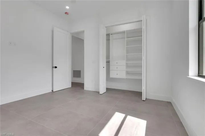 Spacious room featuring light gray tile flooring, crisp white walls, a built-in closet organization system with shelving and drawers, a large window, and a modern interior door with black hardware