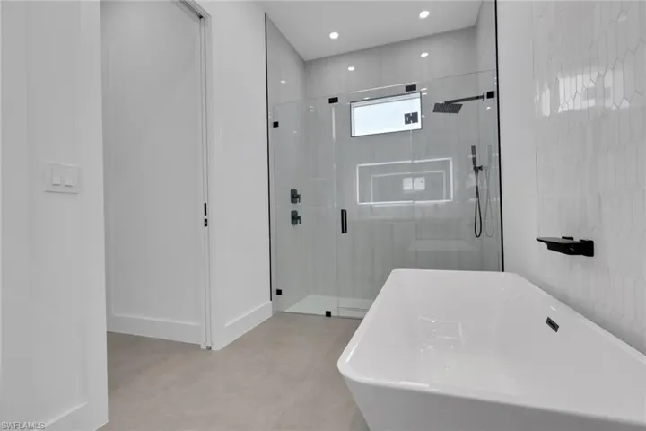 Modern bathroom featuring a freestanding tub, glass-enclosed shower with matte black fixtures, and light-toned geometric tile work
