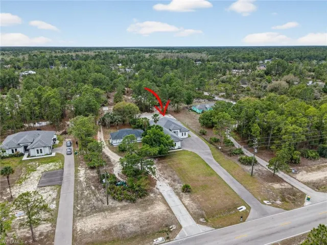 Aerial view showcasing a property with a light-colored exterior and dark roof, set among mature trees