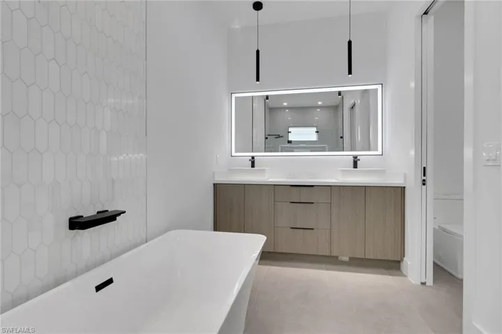Freestanding soaking tub with a black bath shelf, complemented by a white elongated hexagonal tile wall
