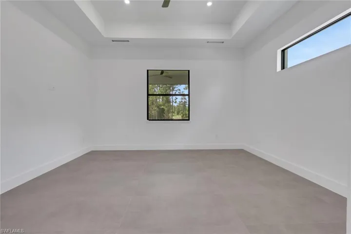 Spacious interior featuring neutral tile flooring, white walls, and a tray ceiling with recessed lighting