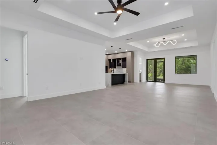 Spacious interior featuring large format tile flooring, tray ceilings with recessed lighting, and a contemporary ceiling fan