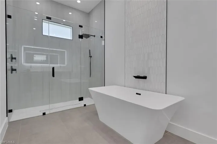 Contemporary bathroom featuring a freestanding soaking tub with a wall-mounted faucet, a glass-enclosed shower with matte black fixtures, an elongated hexagonal tile accent wall, and large format floor tiles