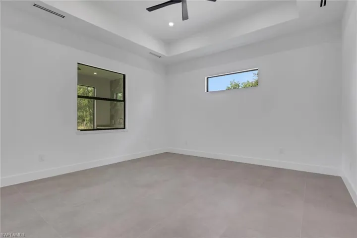Spacious room featuring light-toned tile flooring, white walls, and a tray ceiling