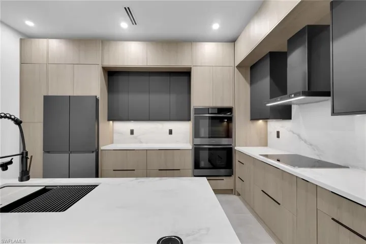 Modern kitchen featuring light wood-finish cabinetry, white countertops with natural veining, and integrated matte black appliances