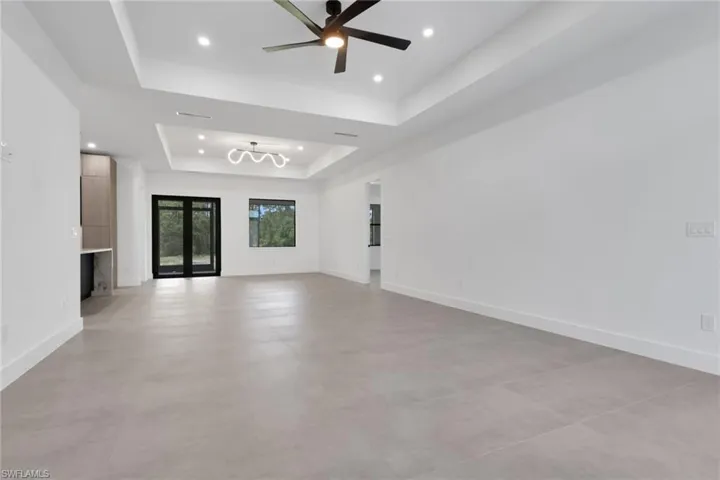 Spacious room featuring light gray tile flooring, white walls, and a tray ceiling with recessed lighting