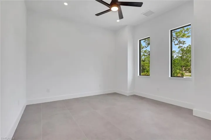 Bright interior space featuring two tall windows, a ceiling fan with integrated lighting, recessed ceiling lights, and light-toned tile flooring