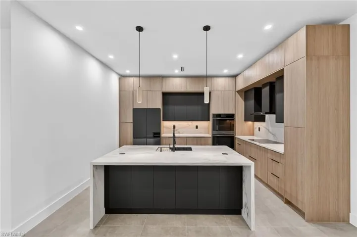 Contemporary kitchen featuring a large island with a waterfall countertop, integrated black sink, and two pendant lights