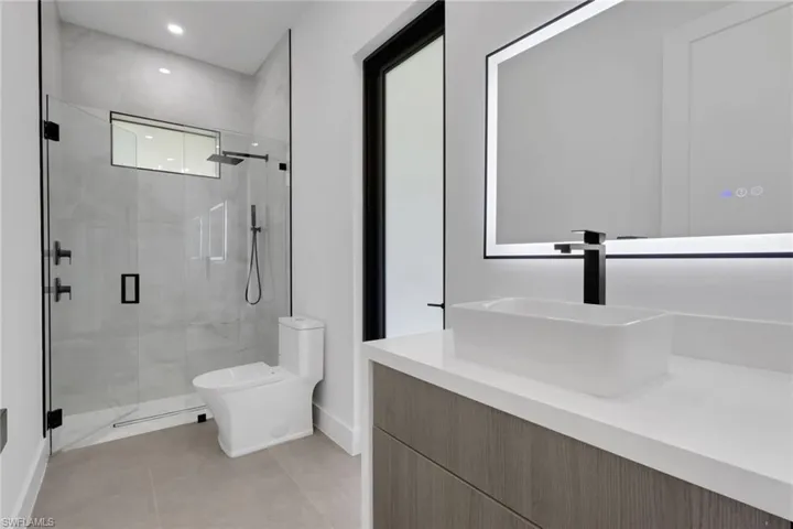 Modern bathroom featuring a glass-enclosed shower, rain shower head, matte black fixtures, a rectangular vessel sink, and an illuminated mirror