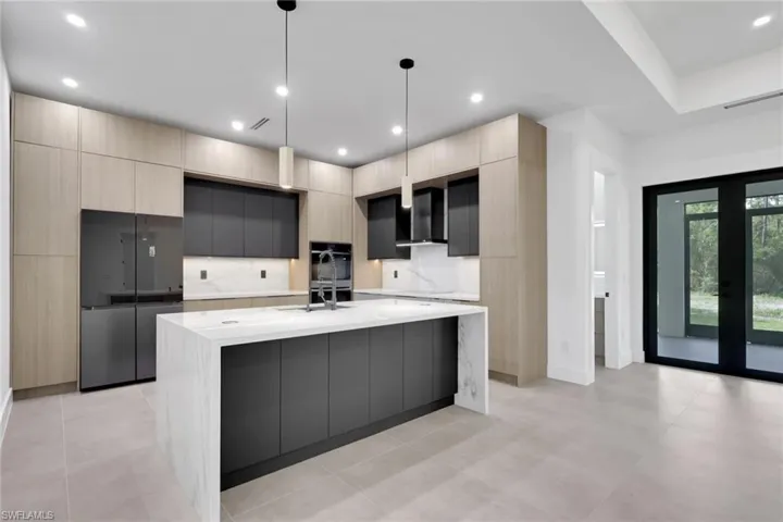 Modern kitchen featuring a waterfall island with a light stone countertop, flat-panel cabinetry in a two-tone finish, integrated refrigerator, and built-in wall oven