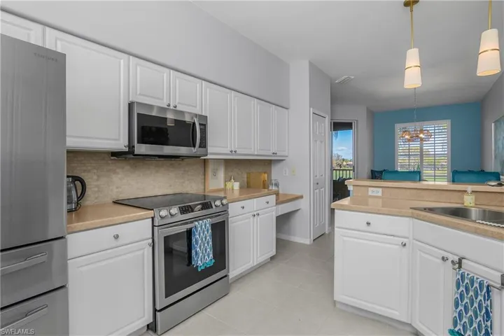 Kitchen with appliances with stainless steel finishes, white cabinetry, a chandelier, decorative light fixtures, and light countertops