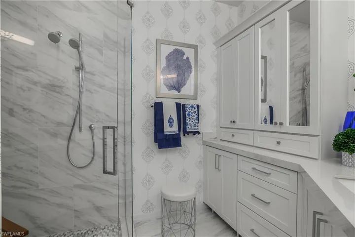 Primary Bathroom featuring a shower stall, wallpapered walls, and vanity