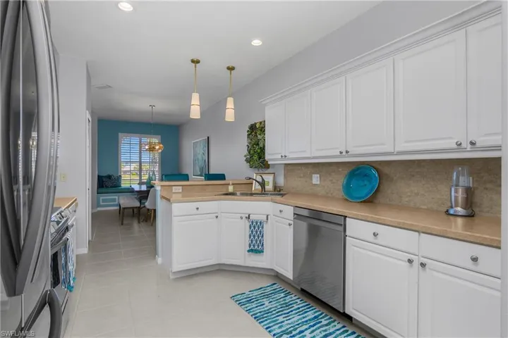 Kitchen with appliances with stainless steel finishes, white cabinets, decorative light fixtures, a peninsula, and light countertops