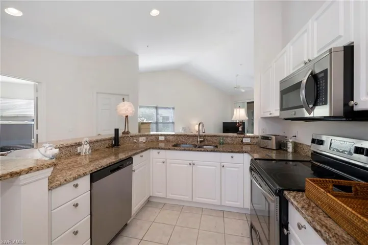 Kitchen featuring stainless steel appliances, light tile floors, sink, lofted ceiling, and white cabinetry