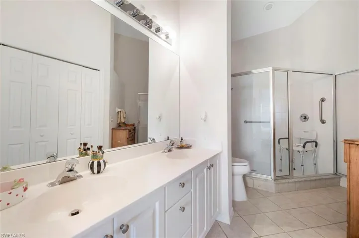 Bathroom with dual sinks, vanity with extensive cabinet space, a shower with door, tile floors, and toilet
