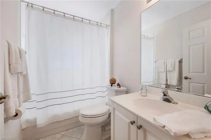 Full bathroom with shower / bath combo with shower curtain, toilet, tile floors, and large vanity