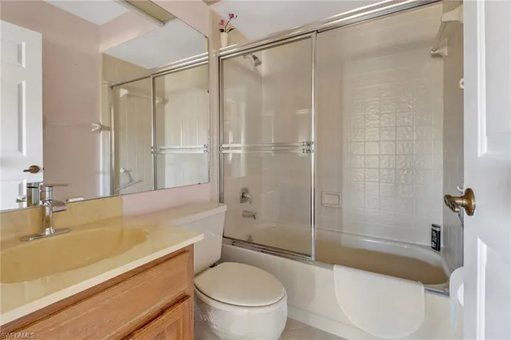 Full bathroom with enclosed tub / shower combo, vanity, and toilet